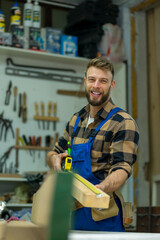 Portrait of young handsome caucasian carpenter who measures a board and smiling for camera