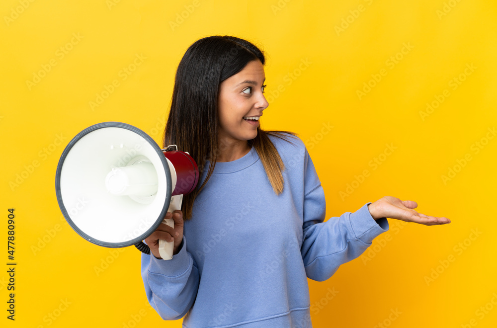 Poster caucasian girl isolated on yellow background holding a megaphone and with surprise facial expression