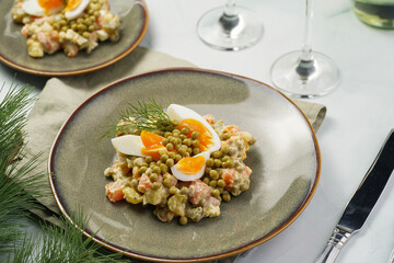 traditional east european dish for New Year's Eve - salad "Olivier" with potatoes, carrots, onion, peas, sausage eggs and mayonnaise on a green plate