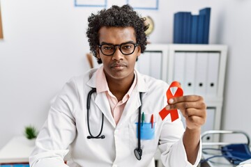 African doctor man holding support red ribbon thinking attitude and sober expression looking self confident - obrazy, fototapety, plakaty