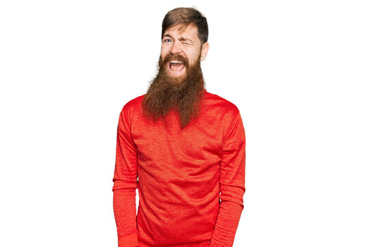 Redhead man with long beard wearing casual clothes winking looking at the camera with sexy expression, cheerful and happy face.
