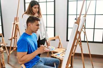 Student and teacher with serious expression painting at art school.