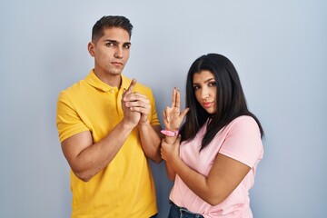 Young couple standing over isolated background holding symbolic gun with hand gesture, playing killing shooting weapons, angry face