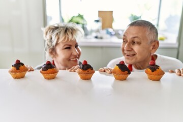 Senior caucasian couple smiling happy smelling baked muffins at the kitchen.