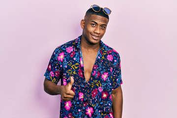 Young black man wearing hawaiian shirt and sunglasses doing happy thumbs up gesture with hand....