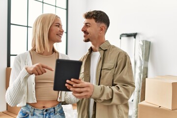 Obraz premium Young caucasian couple smiling happy using touchpad standing at new home.