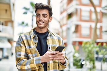 Handsome hispanic man smiling happy and confident at the city using smartphone