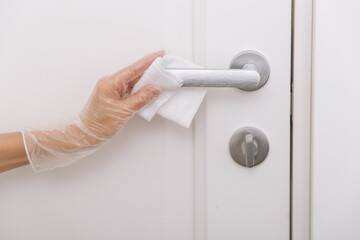 Naklejka premium Cleaning door handles with wet wipe and white gloves. Sanitize surfaces prevention in hospital and public spaces against corona virus. Woman hand using towel for cleaning home room door link.