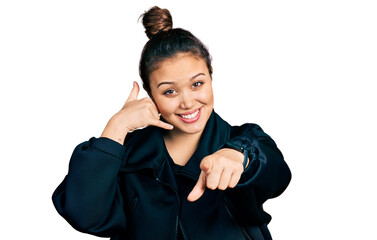 Young hispanic girl wearing sportswear smiling doing talking on the telephone gesture and pointing...