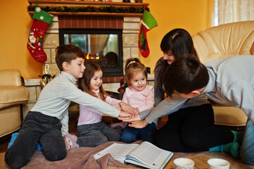 Happy young large family at home by a fireplace in warm living room on winter day.