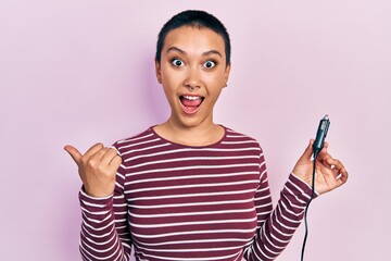 Beautiful hispanic woman with short hair holding usb charger adapter for the car pointing thumb up...