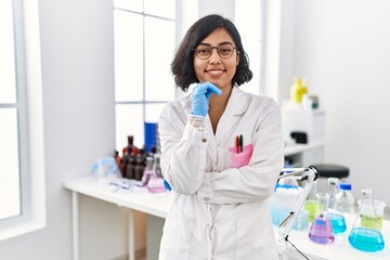 Young latin woman wearing scientist uniform standing at laboratory