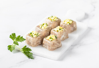 Cold appetizer. Pork jelly with pieces of meat in the form of small square portions with a filling of finely chopped egg and parsley, on a serving board on a white background