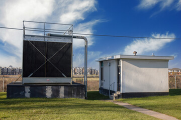 Grey and black steel air conditioning cooling tower next to a low flat stucco control building in...