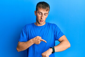 Young caucasian man wearing casual blue t shirt in hurry pointing to watch time, impatience, upset...