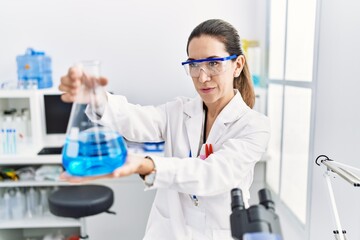 Fototapeta premium Young hispanic woman wearing scientist uniform holding test tube at laboratory