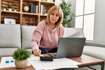 Middle age blonde woman concentrated teleworking sitting on the sofa at home.