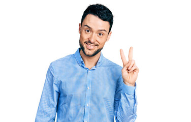 Fototapeta premium Hispanic man with beard wearing casual business shirt smiling with happy face winking at the camera doing victory sign. number two.
