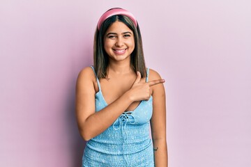Young latin woman wearing summer clothes cheerful with a smile of face pointing with hand and finger up to the side with happy and natural expression on face