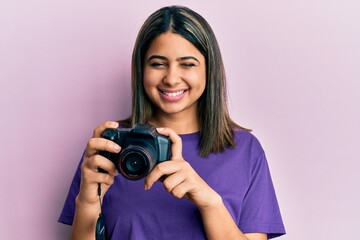 Young latin woman using reflex camera winking looking at the camera with sexy expression, cheerful...