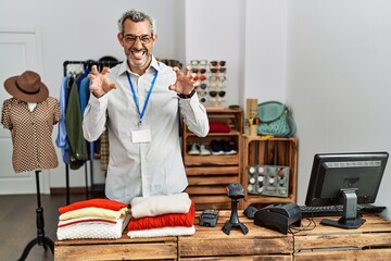 Middle age hispanic man working as manager at retail boutique smiling funny doing claw gesture as...