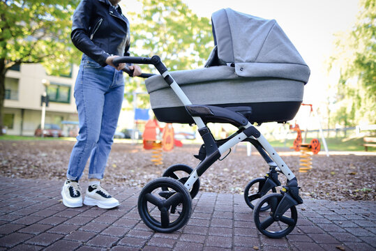 Woman with baby stroller walks in the park. Daily outside walking. Infant sleeping and breathing fresh air in summer.