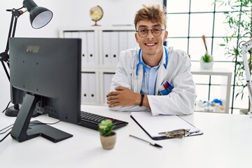 Young caucasian doctor man working at the clinic happy face smiling with crossed arms looking at the camera. positive person.