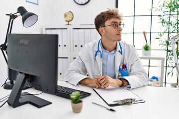 Young caucasian doctor man working at the clinic looking away to side with smile on face, natural expression. laughing confident.