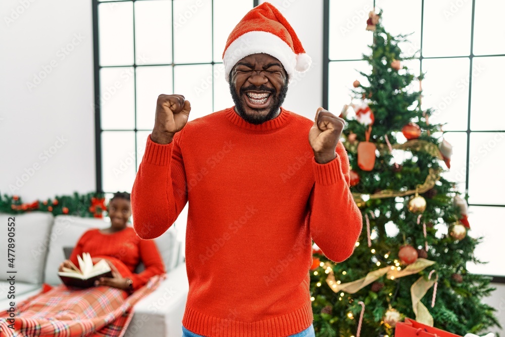 Canvas Prints Young african american man standing by christmas tree celebrating mad and crazy for success with arms raised and closed eyes screaming excited. winner concept