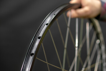A bicycle mechanic holds a bicycle wheel in his hand on a black background. The rim and the specialist's hand are close-up. Bicycle repair.