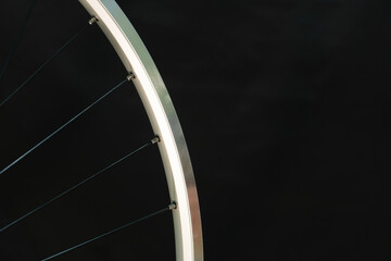 Obraz premium A bicycle wheel without a tire on a black background in the workshop. Bicycle repair. Rim and spokes of a mountain bike wheel close-up.
