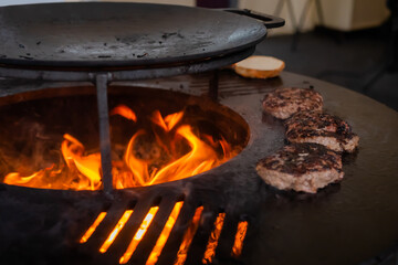 Process of grilling fresh meat cutlets for burgers on brazier with hot flame at summer local food market - close up view. Outdoor cooking, gastronomy, cookery, street food concept