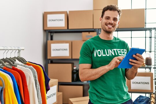 Young hispanic man wearing volunteer uniform using touchpad at charity center - Powered by Adobe