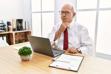 Naklejka premium Senior man working at the office using computer laptop thinking concentrated about doubt with finger on chin and looking up wondering