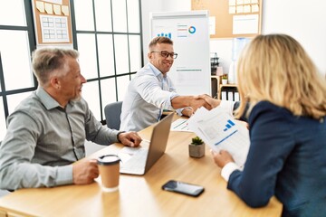 Group of middle age business workers smiling and looking partners handshake at the office.