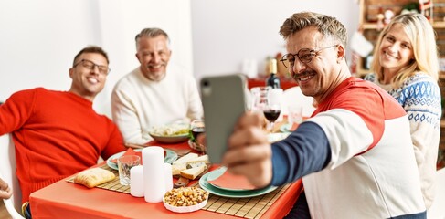 Group of middle age friends smiling happy having christmas dinner and making selfie by the smartphone at home.