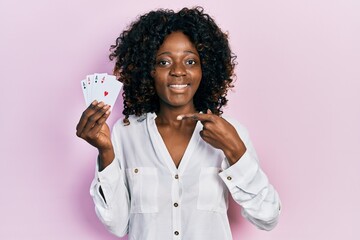 Young african american woman playing poker holding cards smiling happy pointing with hand and finger