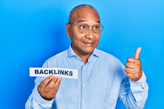 Middle age latin man holding paper with backlinks message pointing thumb up to the side smiling happy with open mouth