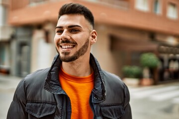 Handsome hispanic man with beard smiling happy and confident at the city wearing winter coat
