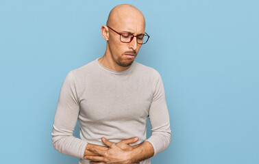 Bald man with beard wearing casual clothes and glasses with hand on stomach because indigestion,...