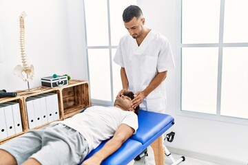Two hispanic men physiotherapist and patient having rehab session massaging head at clinic