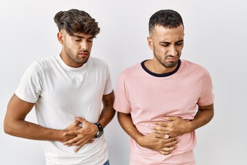Young gay couple standing over isolated background with hand on stomach because indigestion, painful illness feeling unwell. ache concept.