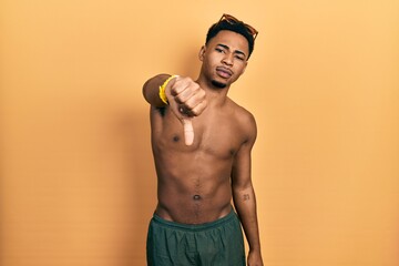 Young african american man wearing swimwear and swimmer glasses looking unhappy and angry showing...