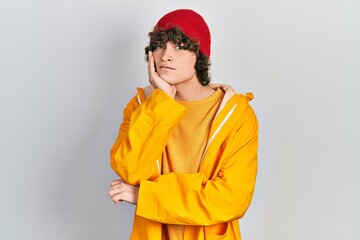 Handsome young man wearing yellow raincoat thinking looking tired and bored with depression problems with crossed arms.