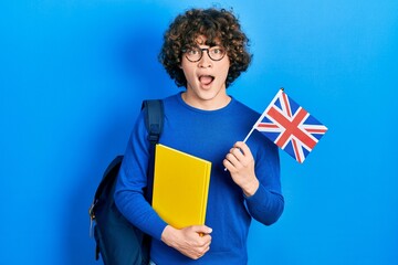 Handsome young man exchange student holding uk flag celebrating crazy and amazed for success with open eyes screaming excited. - obrazy, fototapety, plakaty