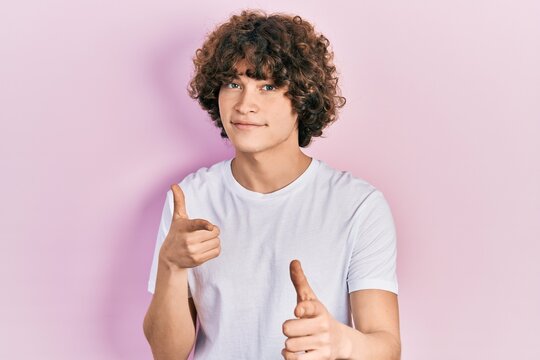 Handsome young man wearing casual white t shirt pointing fingers to camera with happy and funny face. good energy and vibes.