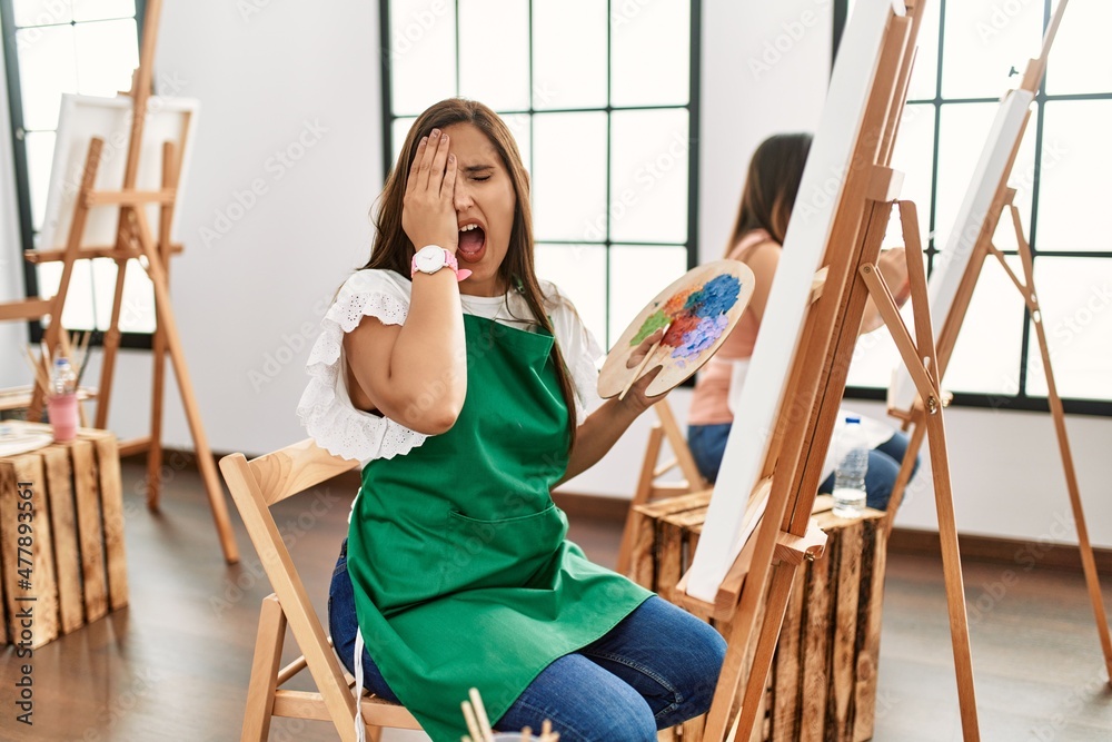 Sticker Young hispanic artist women painting on canvas at art studio yawning tired covering half face, eye and mouth with hand. face hurts in pain.