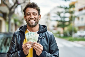 Fotobehang Handsome hispanic man with beard holding 500 argentina pesos banknotes outdoors © Krakenimages.com