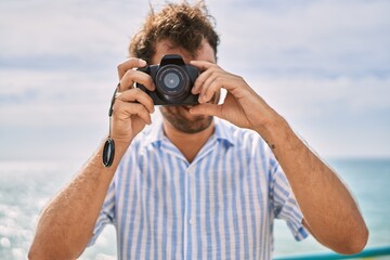 Obraz premium Young hispanic man smiling happy using camera at the beach.