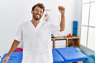 Young handsome physiotherapist man working at pain recovery clinic dancing happy and cheerful, smiling moving casual and confident listening to music